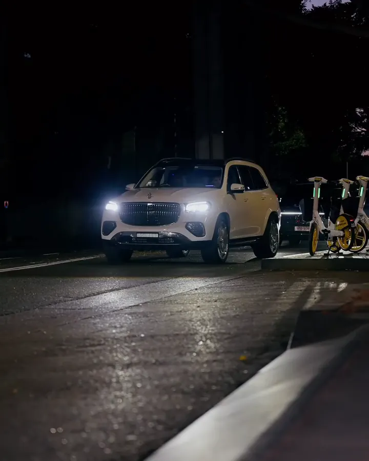 A white Maybach GLS pulling in at night, headlights on
