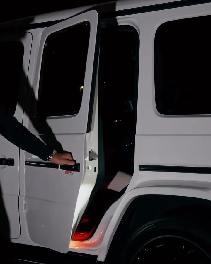 A chauffeur opening the rear door of a white Mercedes G-Wagon at night
