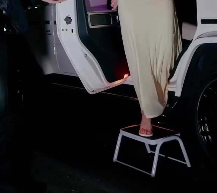 A guest in a long gown stepping down onto a step at the door of a white G-Wagon