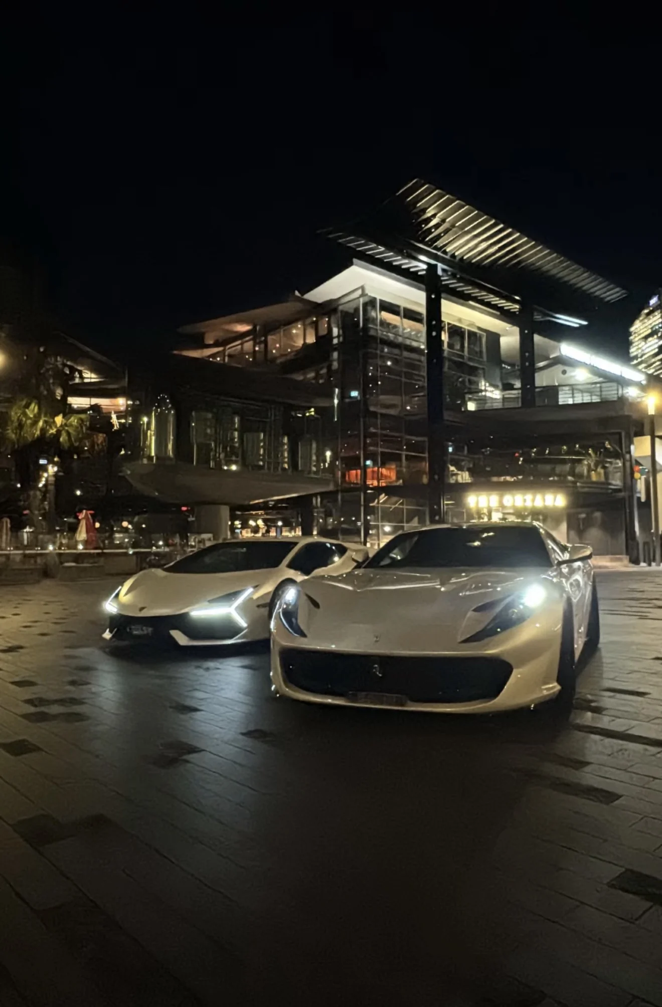 A Ferrari from the G Class Hire fleet photographed at night on a wet Sydney street, the building lights reflected in the road