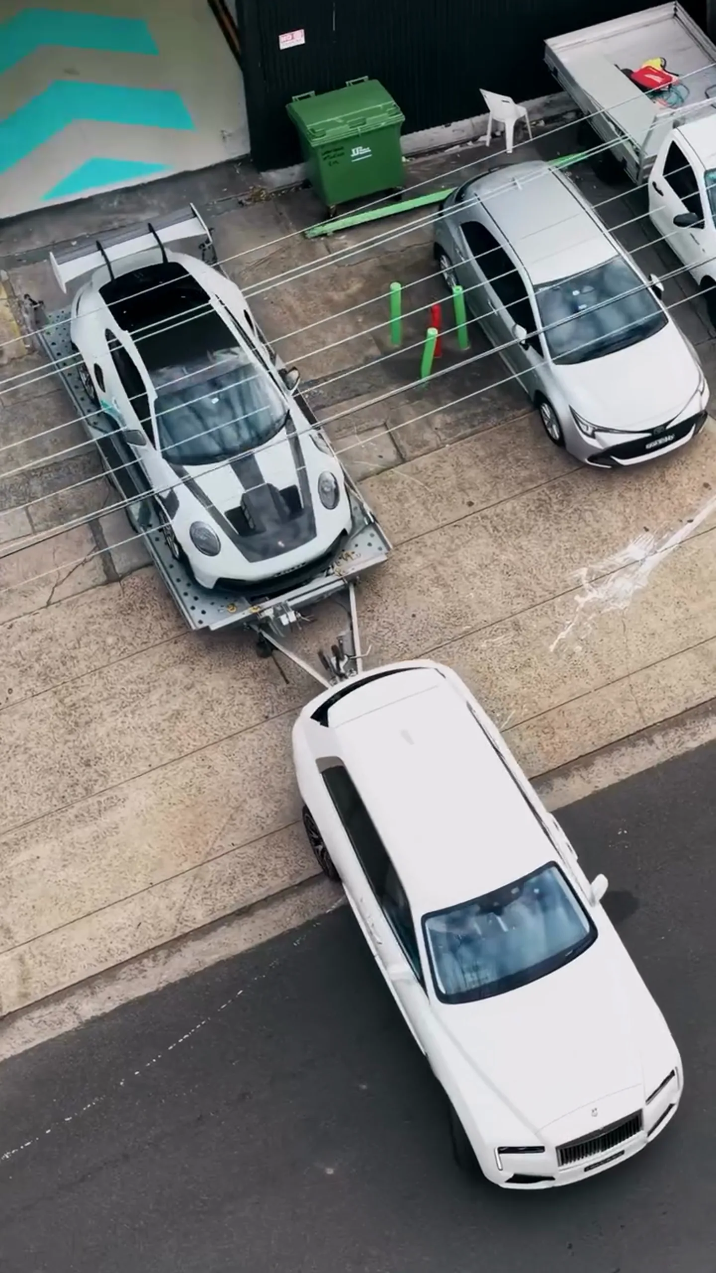 A Rolls-Royce Cullinan towing a trailer loaded with a Porsche 911 GT3 RS, seen from above in Sydney