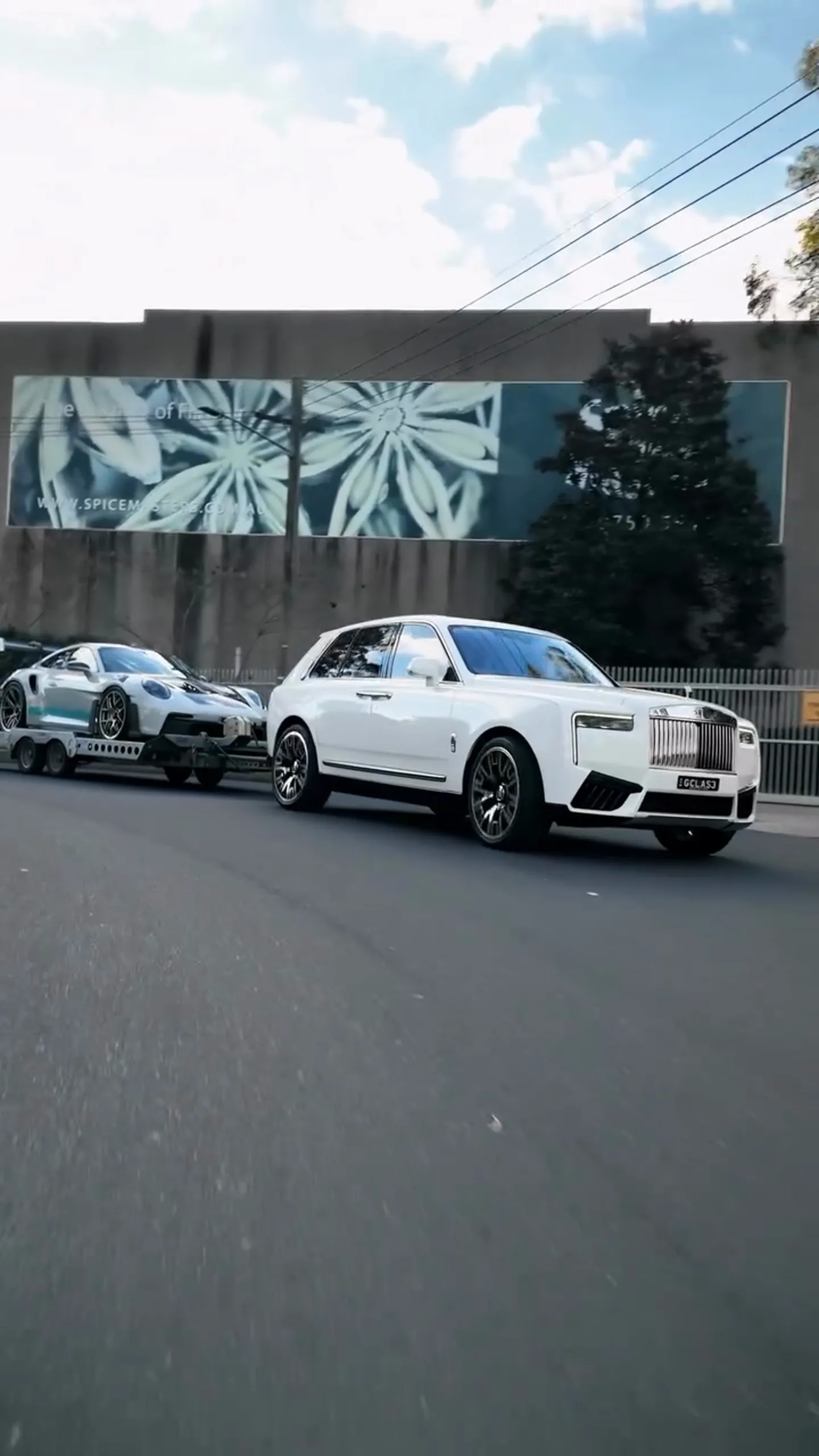 A Rolls-Royce Cullinan, towing a supercar across Sydney